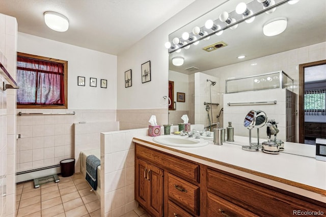 bathroom with a baseboard heating unit, tile patterned floors, vanity, a shower with shower door, and tile walls