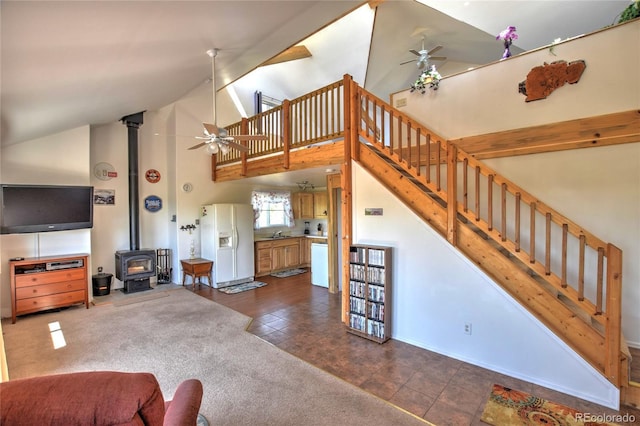 living room featuring a wood stove, high vaulted ceiling, carpet flooring, ceiling fan, and stairs