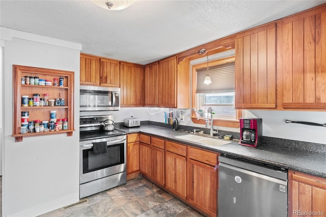 kitchen featuring sink, hanging light fixtures, a textured ceiling, and appliances with stainless steel finishes