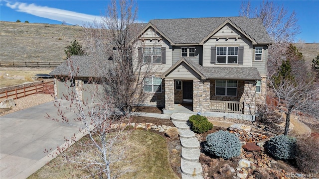 craftsman house featuring stone siding, a porch, fence, concrete driveway, and a shingled roof