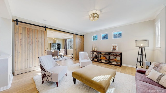 living area with a barn door, light wood-style floors, ornamental molding, and a notable chandelier