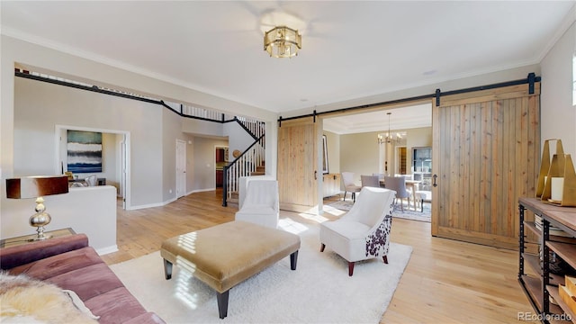 living area with a barn door, stairway, ornamental molding, and light wood-style flooring