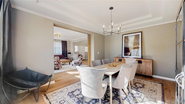 dining space with baseboards, a raised ceiling, an inviting chandelier, and wood finished floors