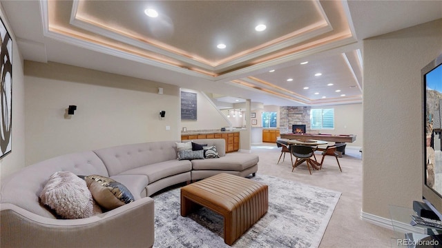 living room with a raised ceiling, light colored carpet, ornamental molding, and a fireplace