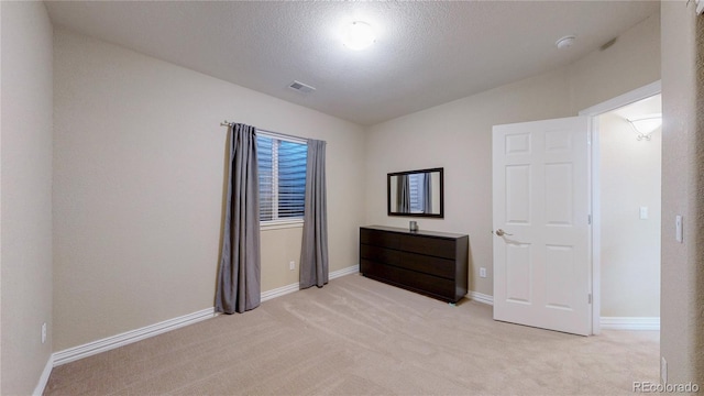 unfurnished bedroom featuring visible vents, light colored carpet, a textured ceiling, and baseboards