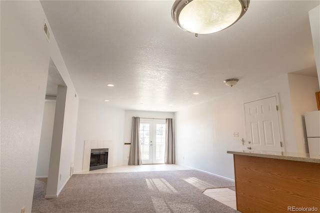 unfurnished living room featuring light colored carpet, a textured ceiling, a tile fireplace, and french doors