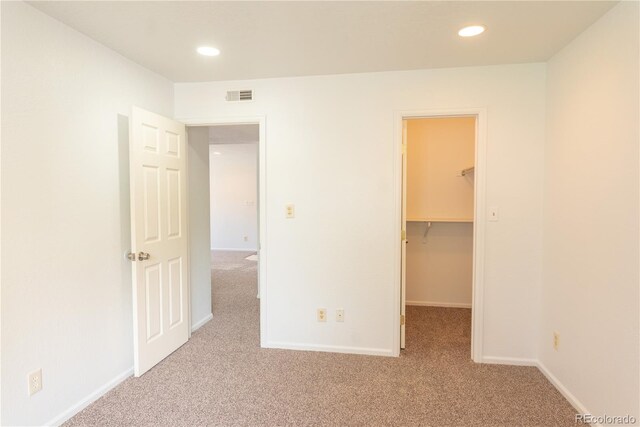 unfurnished bedroom featuring a spacious closet, a closet, and light carpet