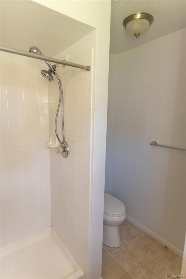 bathroom with toilet, tile patterned flooring, and tiled shower