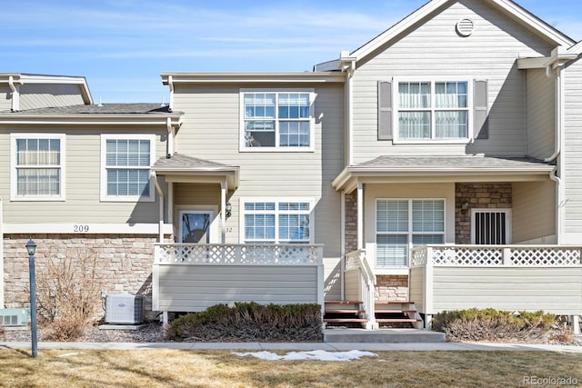 view of front of home featuring cooling unit, stone siding, and roof with shingles