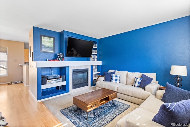 living room with built in shelves, baseboards, wood finished floors, and a tile fireplace