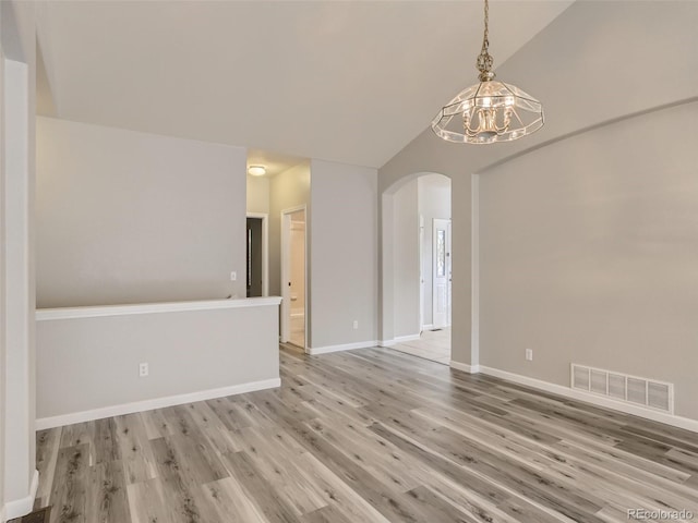 unfurnished room featuring a notable chandelier, arched walkways, baseboards, light wood-type flooring, and visible vents
