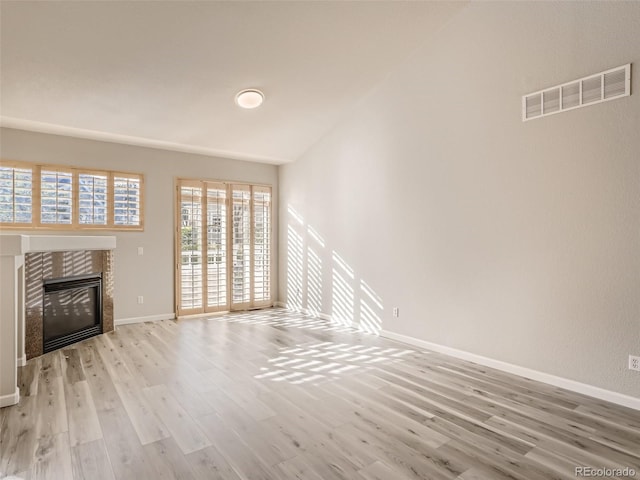 unfurnished living room with visible vents, a tiled fireplace, wood finished floors, baseboards, and lofted ceiling