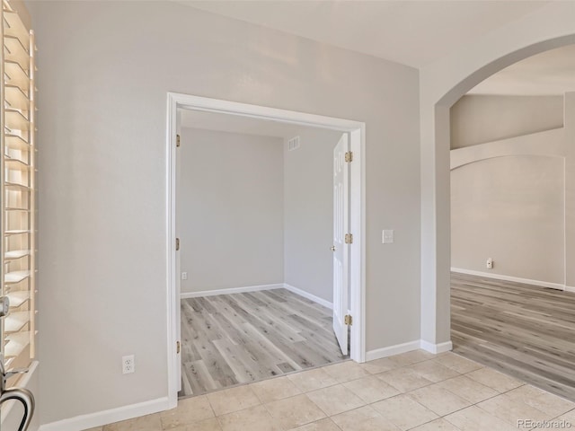 unfurnished room featuring baseboards, arched walkways, tile patterned floors, and visible vents