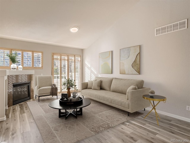 living area featuring visible vents, wood finished floors, a fireplace, baseboards, and vaulted ceiling