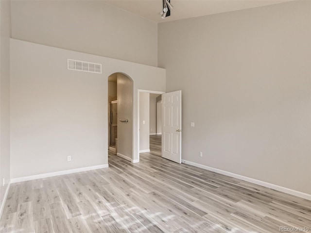 empty room featuring visible vents, a towering ceiling, baseboards, arched walkways, and light wood finished floors