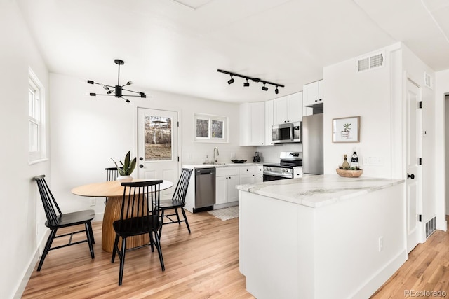 kitchen with visible vents, light wood-style flooring, appliances with stainless steel finishes, a sink, and a peninsula