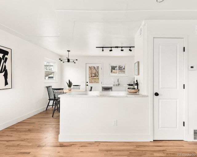 interior space with light wood-style flooring, a peninsula, a sink, visible vents, and baseboards