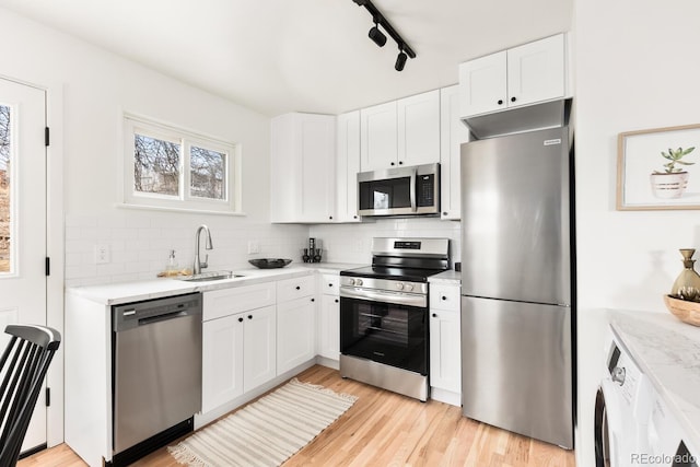 kitchen with white cabinets, light wood-style flooring, a sink, stainless steel appliances, and backsplash