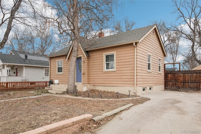 bungalow-style home featuring roof with shingles, concrete driveway, a chimney, and fence