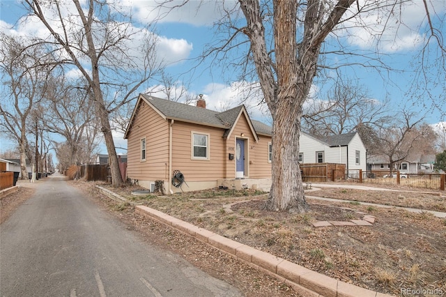 bungalow-style house with a shingled roof, aphalt driveway, fence, and a chimney