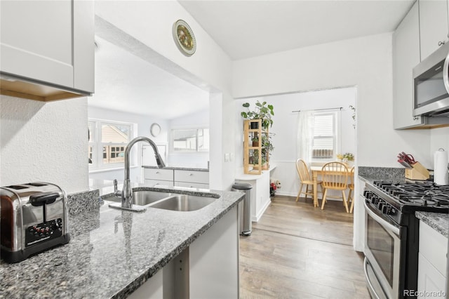 kitchen featuring stone counters, light wood-style flooring, a sink, appliances with stainless steel finishes, and white cabinetry