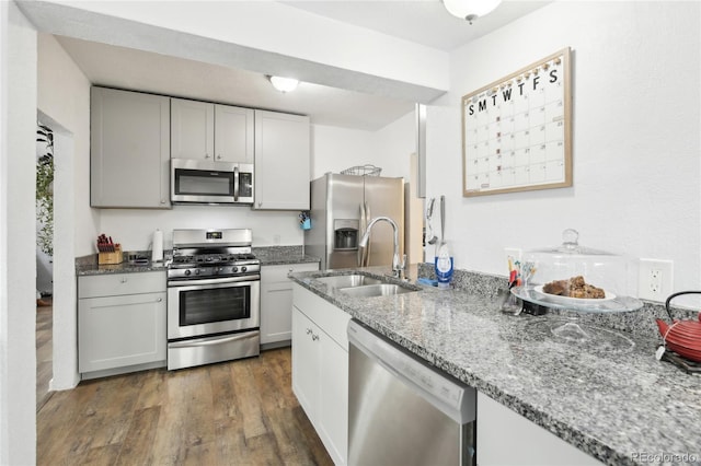 kitchen featuring light stone counters, dark wood-style flooring, appliances with stainless steel finishes, and a sink