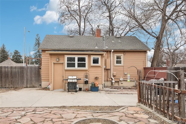 back of property with a shingled roof, a chimney, a patio, and fence