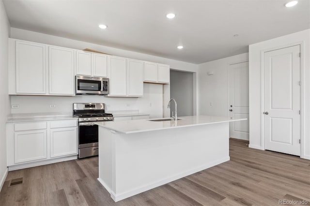 19040 E 96th Pl, Commerce City, CO 80022 - kitchen with stainless steel appliances, a sink, light wood-style floors, white cabinetry, and an island with sink