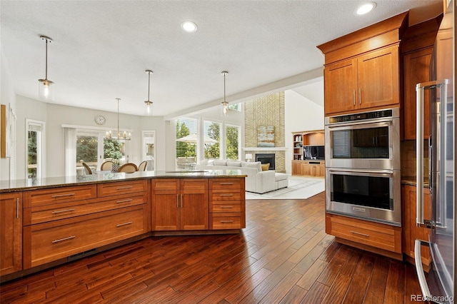 9556 Kemper Dr, Lone Tree, CO 80124 - kitchen featuring stainless steel appliances, brown cabinets, a large fireplace, dark stone counters, and dark wood-style flooring