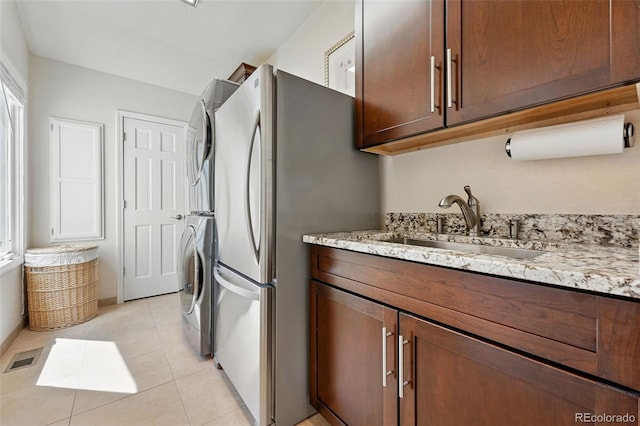 9556 Kemper Dr, Lone Tree, CO 80124 - kitchen featuring estacked washer and dryer, light stone counters, freestanding refrigerator, and light tile patterned floors