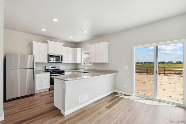 kitchen featuring visible vents, white cabinetry, stainless steel appliances, a peninsula, and light wood finished floors