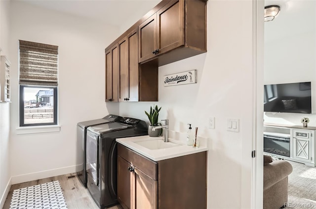 washroom featuring washer and dryer, sink, light hardwood / wood-style flooring, and cabinets