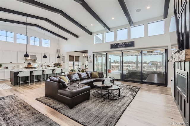 living room featuring beamed ceiling, a healthy amount of sunlight, a notable chandelier, and light hardwood / wood-style floors