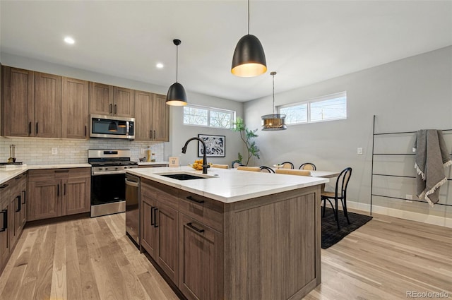 4127 Tejon St, Denver, CO 80211 - kitchen featuring stainless steel appliances, a sink, light wood finished floors, tasteful backsplash, and hanging light fixtures