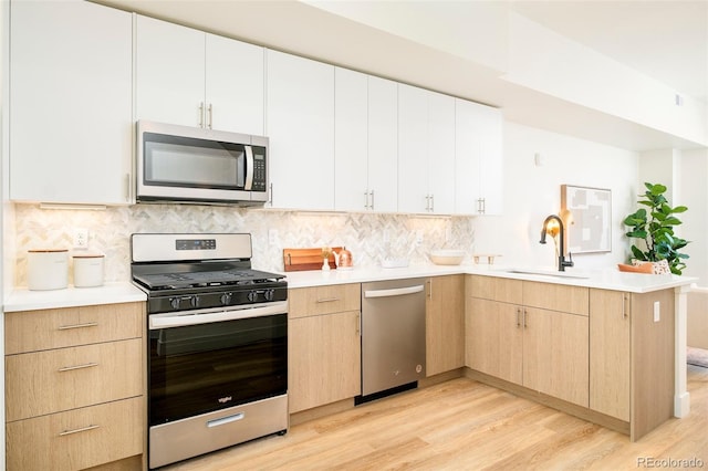kitchen with a peninsula, light brown cabinets, light wood-type flooring, a sink, and appliances with stainless steel finishes