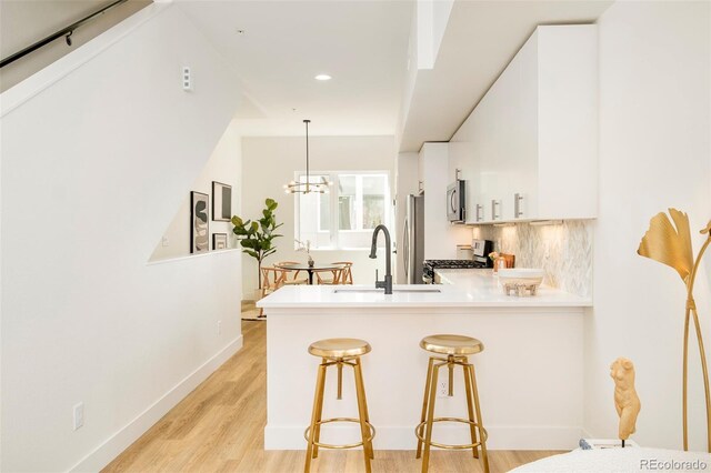 kitchen featuring a sink, white cabinets, a peninsula, light wood-style floors, and stainless steel appliances