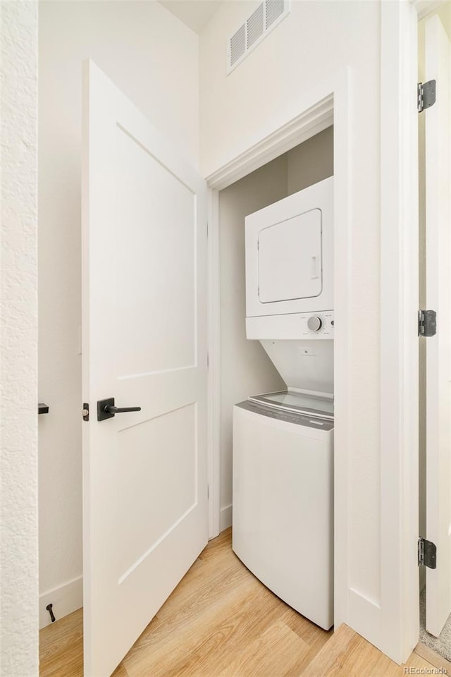 washroom featuring stacked washer / drying machine, visible vents, and light wood finished floors