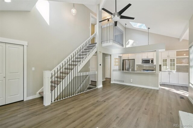 9455 W 81st Ave Unit A, Arvada, CO 80005 - unfurnished living room featuring high vaulted ceiling, a skylight, wood finished floors, a ceiling fan, and stairs