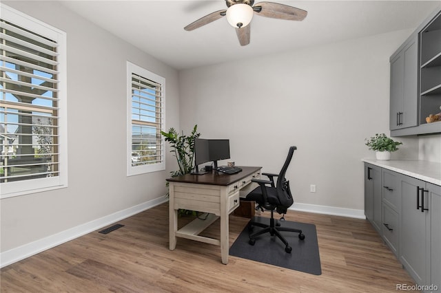 office area with light wood finished floors, baseboards, visible vents, and ceiling fan