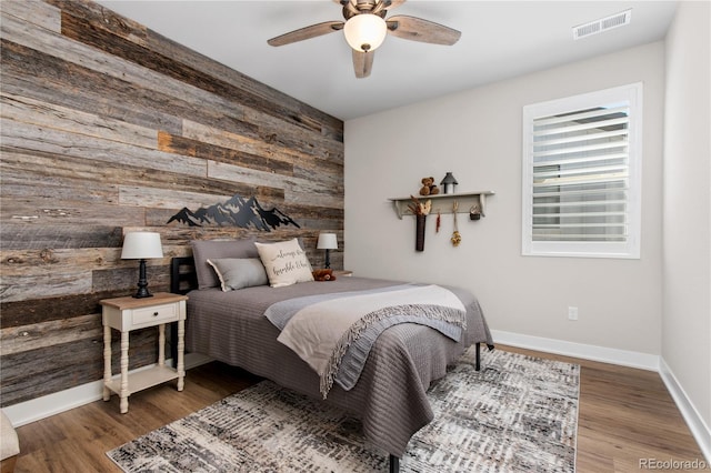 bedroom featuring an accent wall, wood finished floors, visible vents, and wooden walls