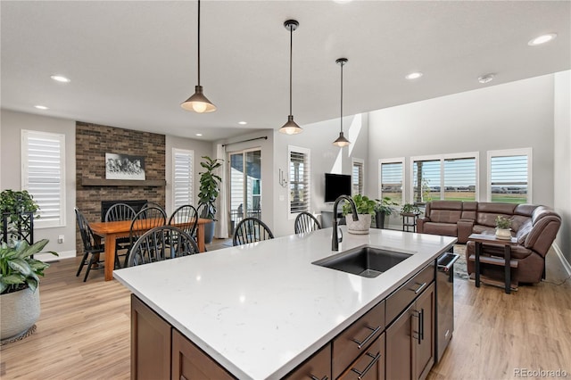 kitchen with decorative light fixtures, light wood-style floors, a brick fireplace, open floor plan, and a sink