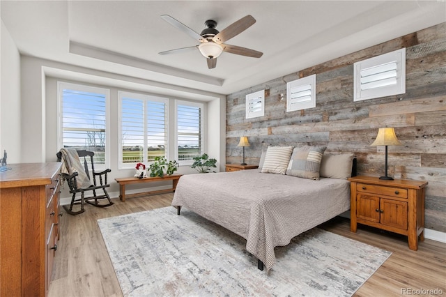 bedroom featuring light wood finished floors, a raised ceiling, and baseboards