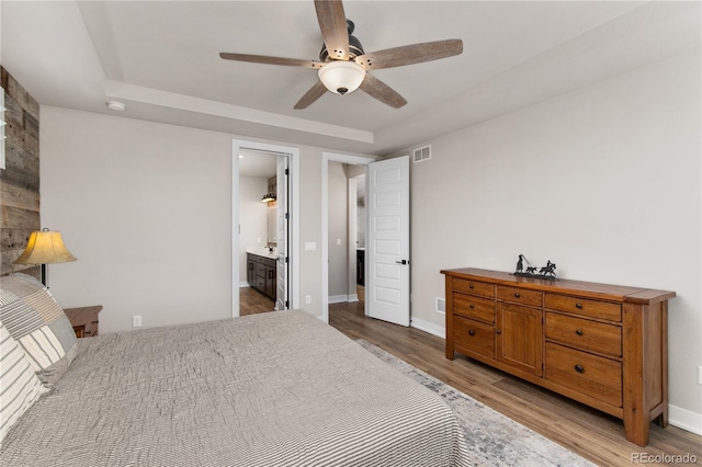 bedroom with baseboards, visible vents, a raised ceiling, and wood finished floors