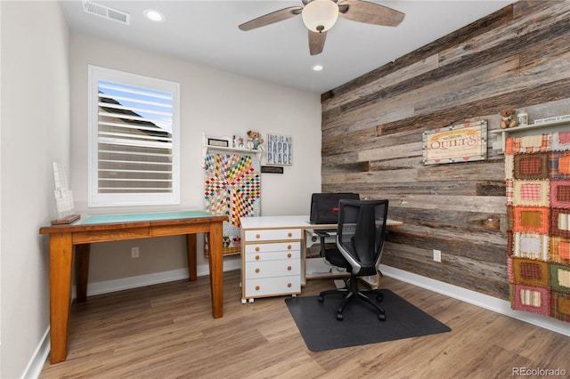 home office with wood walls, light wood-type flooring, visible vents, and baseboards