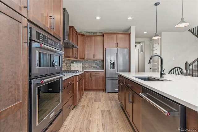 kitchen with stainless steel appliances, a sink, light countertops, backsplash, and wall chimney exhaust hood