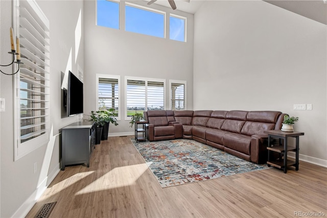 living area featuring light wood-style flooring, a high ceiling, visible vents, baseboards, and a ceiling fan