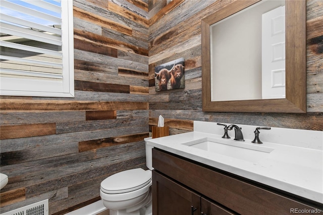 bathroom featuring toilet, wooden walls, visible vents, and vanity