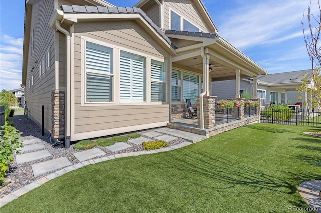 back of property with stone siding, ceiling fan, fence, and a yard