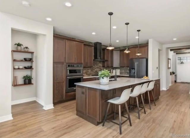 kitchen with high quality fridge, stainless steel double oven, light countertops, wall chimney range hood, and backsplash