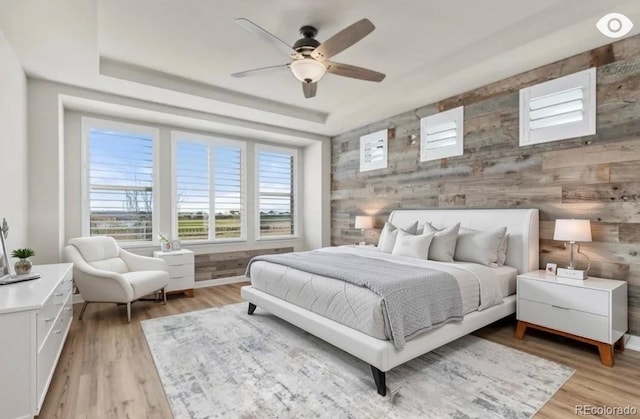 bedroom featuring a ceiling fan, a raised ceiling, baseboards, and light wood finished floors